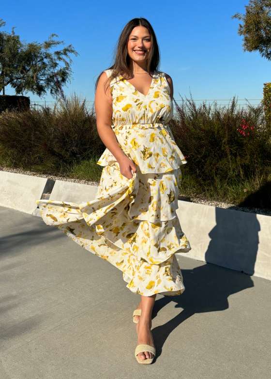Model wearing Stitch Fix women’s clothing, including: a white and yellow floral sleeveless tiered maxi dress, styled with neutral block-heel sandals.