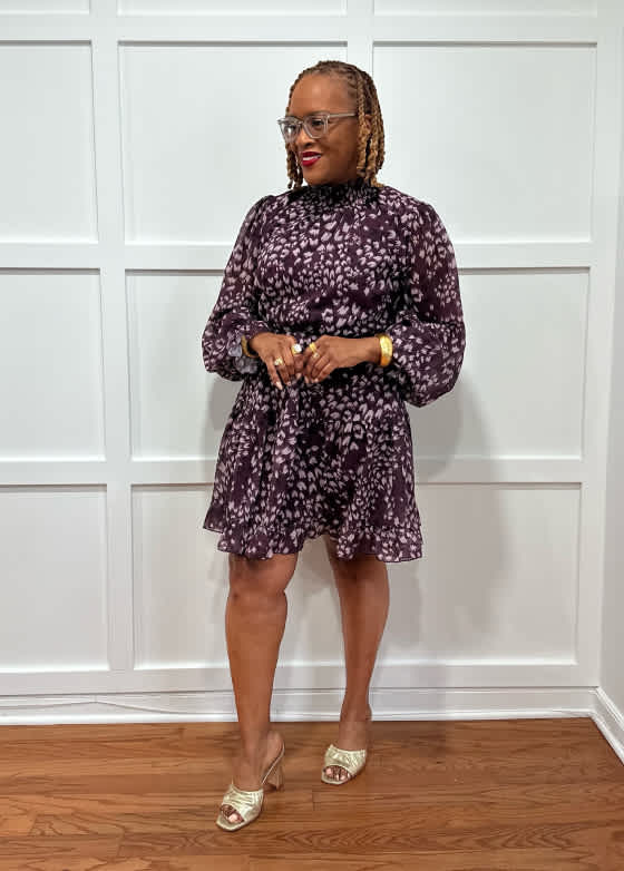 Model wearing Stitch Fix women’s clothing, including: a long-sleeve dark plum mini dress with metallic shimmer and tiered skirt, styled with strappy heels.