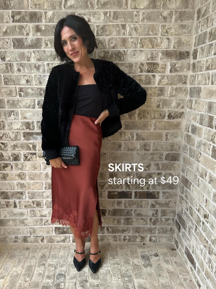 Skirts starting at $49. The image shows a petite woman in a black jacket, a black top, a rust-colored slip skirt with lace trim, black heels and a black clutch