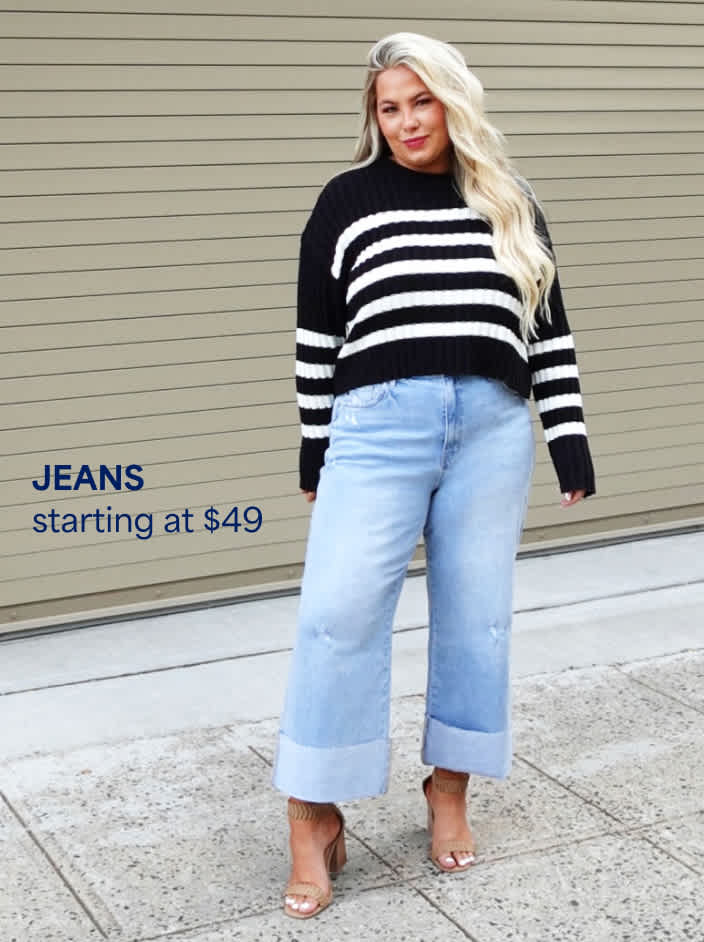 Jeans starting at $49. The image shows a petite woman in a navy and white striped sweater, wide-leg cuffed jeans and bude strappy heels