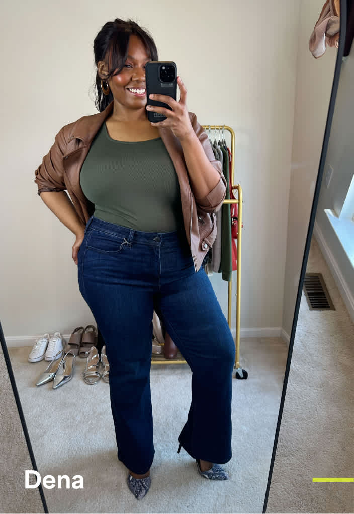 A petite woman with long brown hair wears an olive green bodysuit with dark-wash jeans and high heels and a lightweight brown jacket.