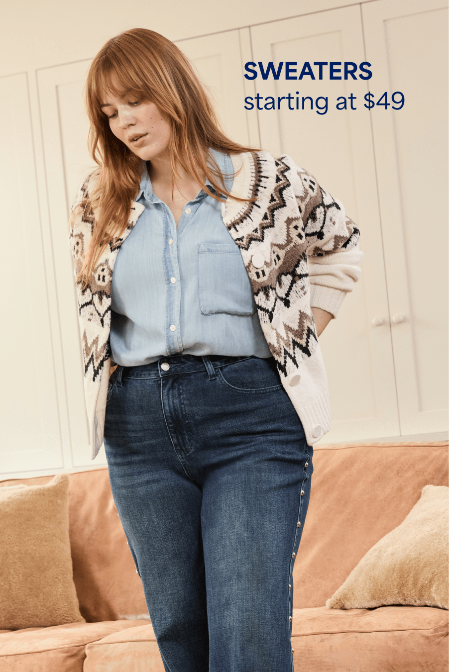 A woman with auburn hair is wearing a blue button-down with dark blue jeans and a cream and brown cardigan with a fair isle design. Sweaters starting at $49