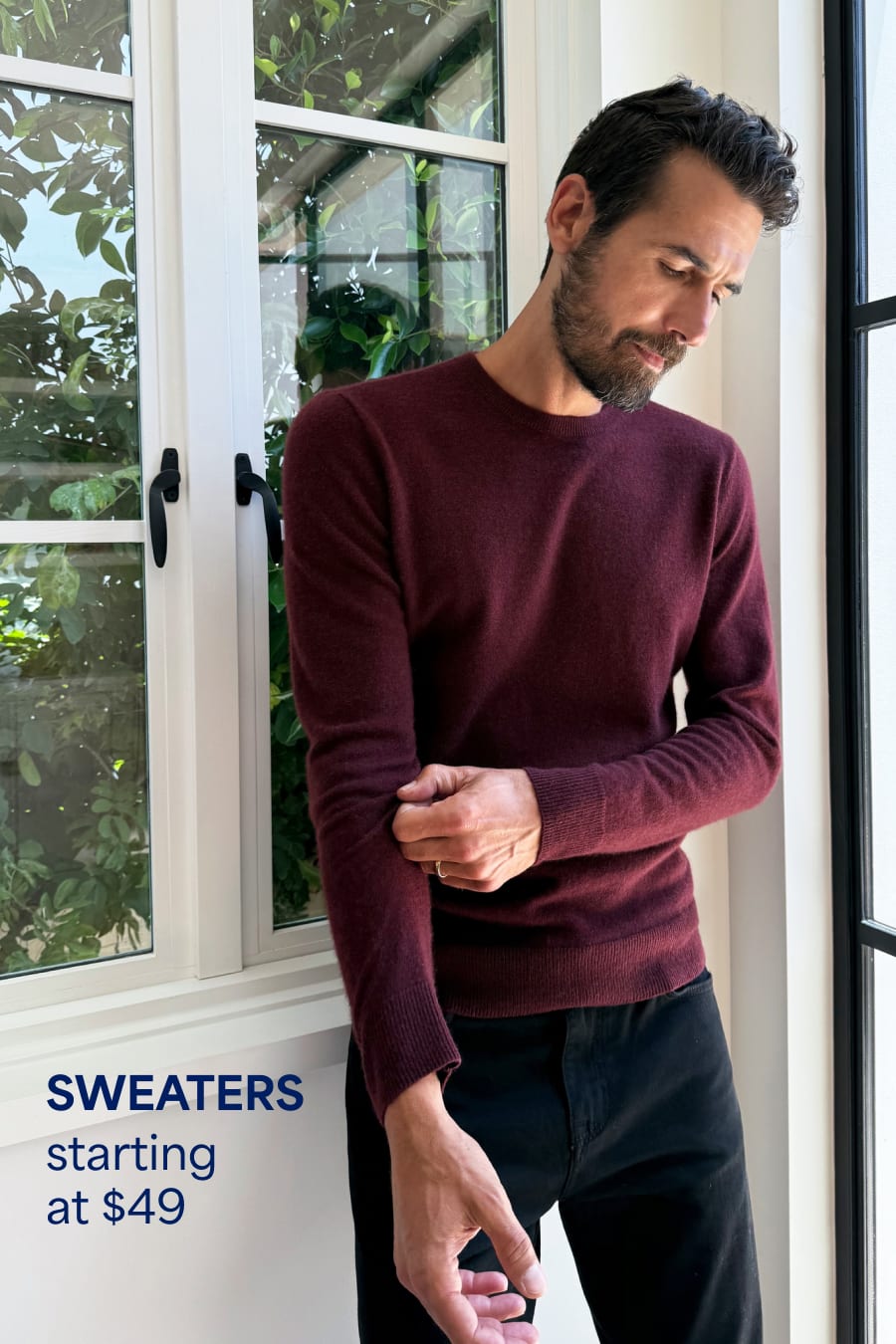 A bearded man wears a burgundy sweater with black pants. Sweaters starting at $49