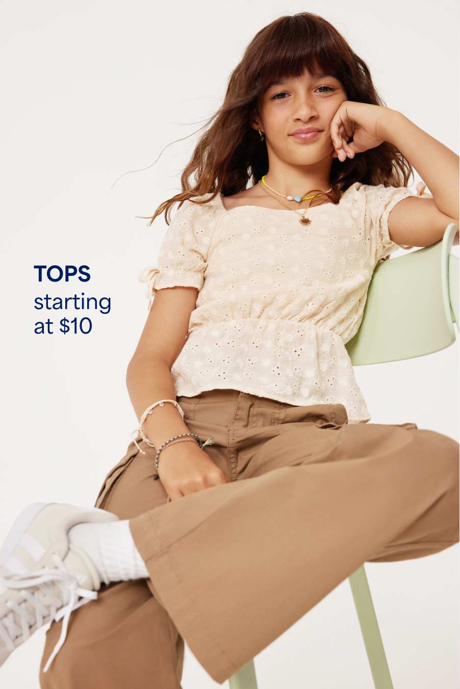 A girl wears a feminine cinch-waist top with tan cargo pants, white socks and white sneakers. Tops starting at $10