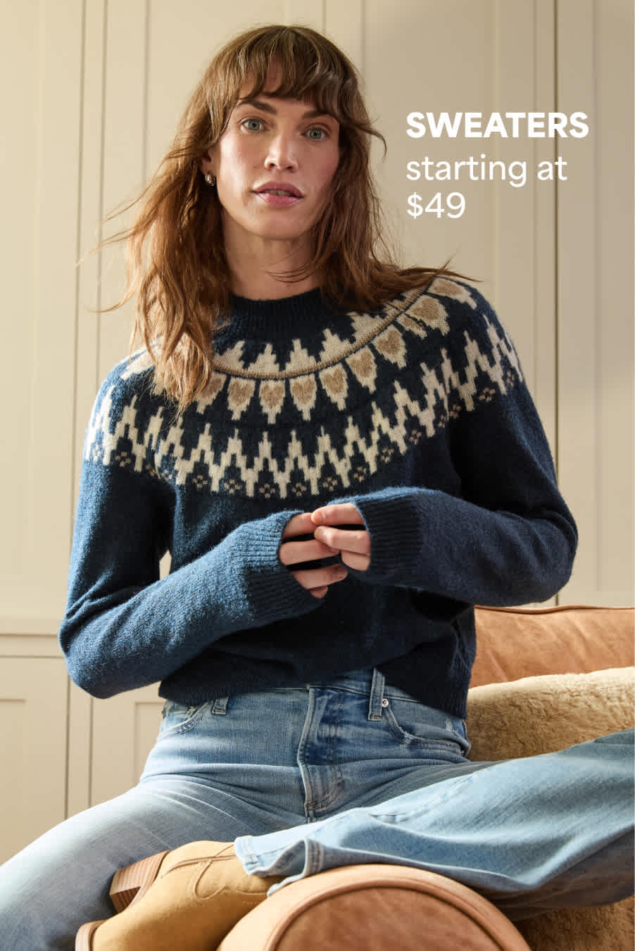 Stitch Fix women’s image showing a woman seated in a cozy space wearing a navy sweater with a Nordic pattern and light denim jeans. Text reads: “SWEATERS starting at $49.”