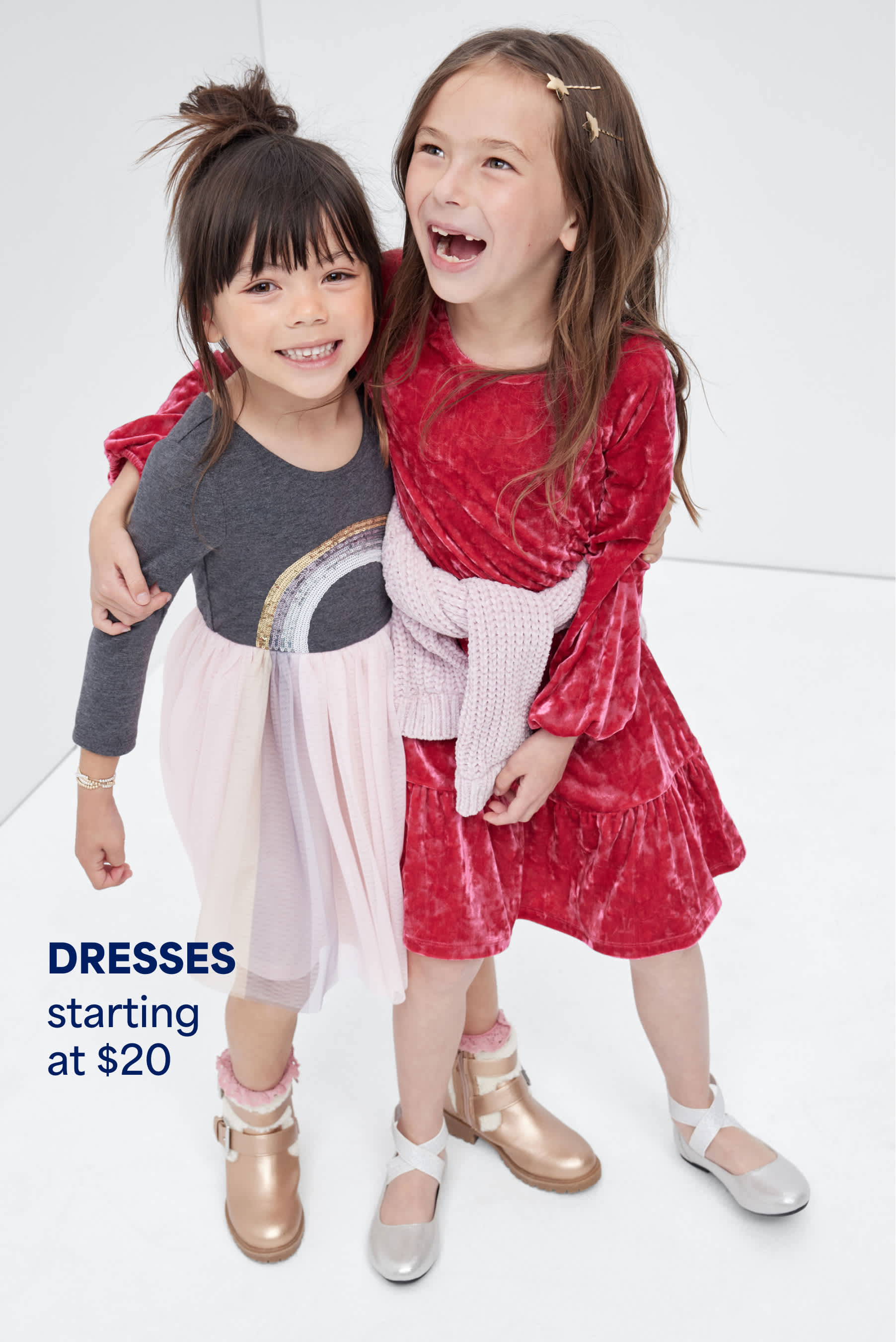 Stitch Fix Kids image featuring two smiling girls hugging, dressed in playful dresses — one in a pink tulle skirt and rainbow top, the other in a red velvet dress. Text reads: “DRESSES starting at $20.”