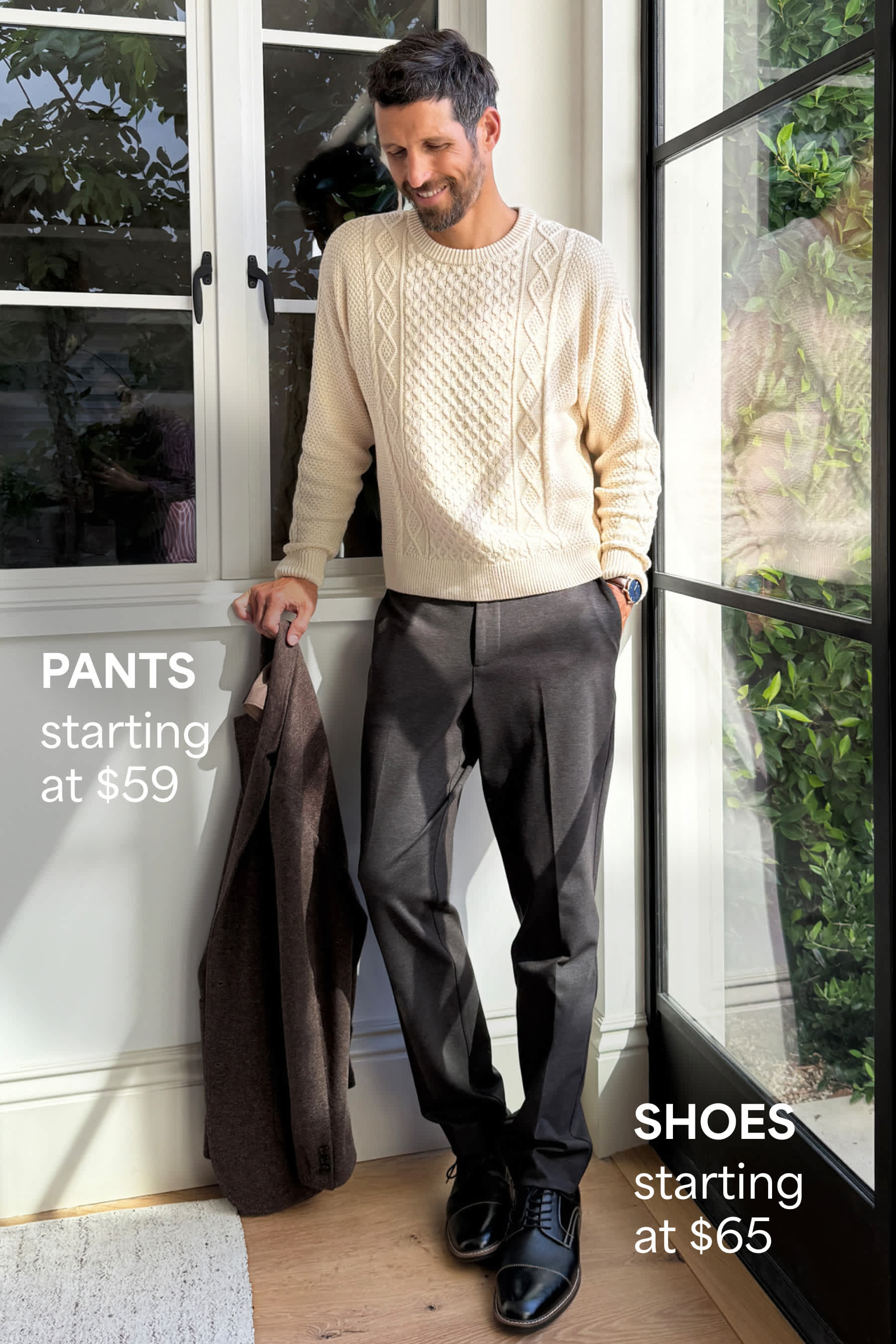 Stitch Fix men’s fashion image showing a man in a cream cable-knit sweater, gray trousers, and black dress shoes, standing by a window. Text reads: “PANTS starting at $59” and “SHOES starting at $65.”