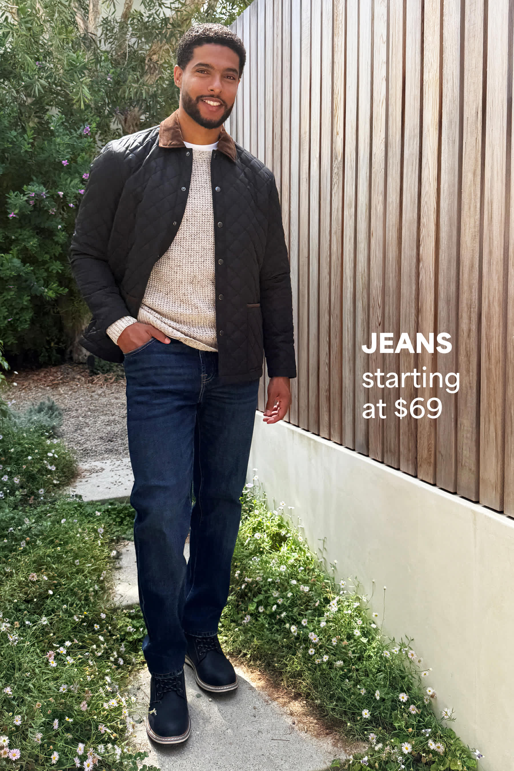 Stitch Fix men’s fashion image featuring a man in a gray bomber jacket, beige sweater, and dark-wash jeans, standing outdoors and smiling. Text reads: “JEANS starting at $69.”