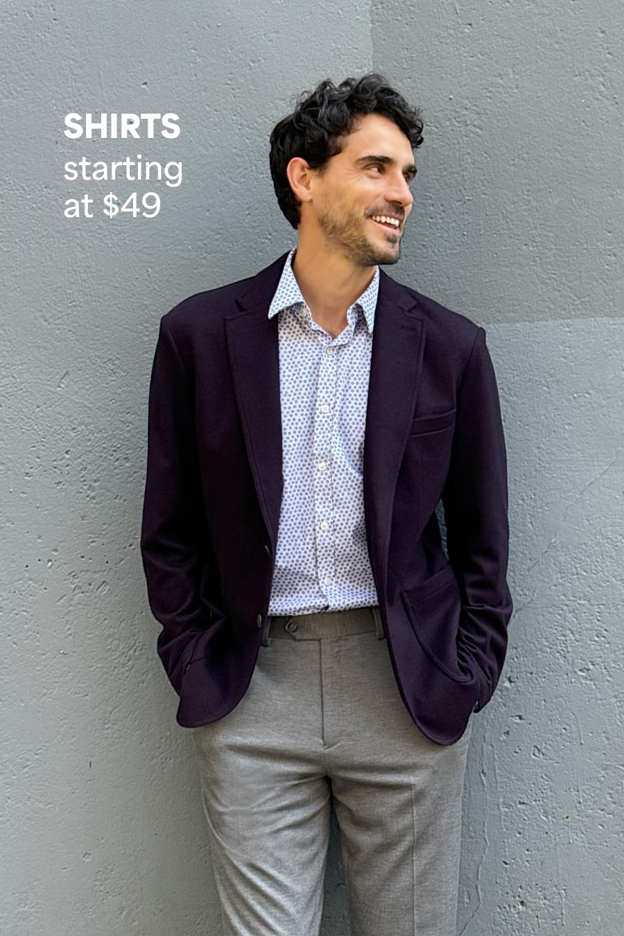 Stitch Fix men’s outfit featuring a man in a plum blazer, light blue printed shirt, and gray pants, leaning casually against a wall. Text reads: “SHIRTS starting at $49.”