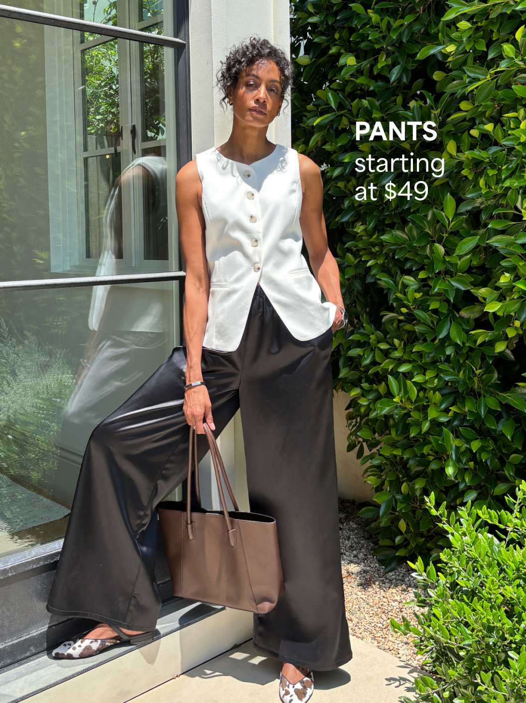 A Stitch Fix woman model posing and wearing satin trousers and a vest. Pants starting at $49