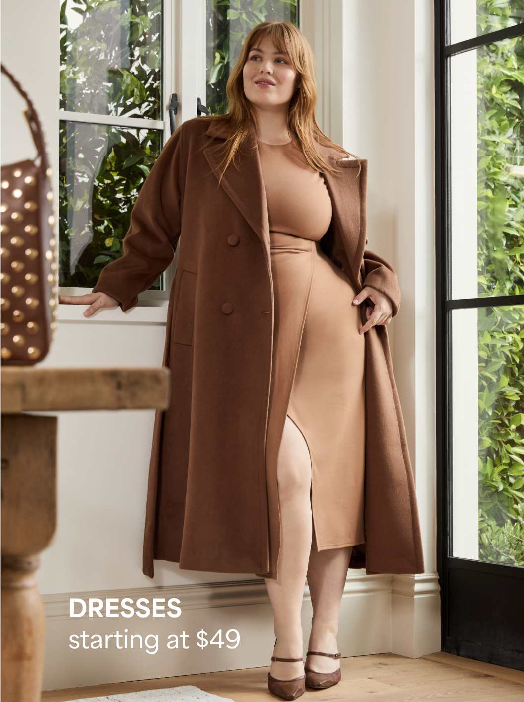 A Stitch Fix woman model posing and wearing a tan dress and matching brown coat. Dresses starting at $49