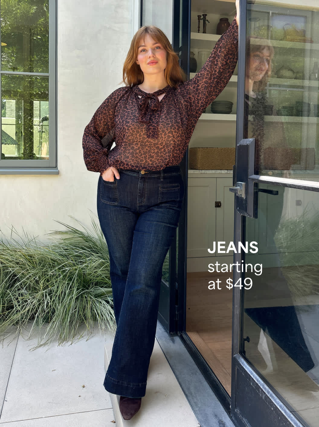 A Stitch Fix woman model posing and wearing dark-wash jeans and a blouse. Jeans starting at $49.