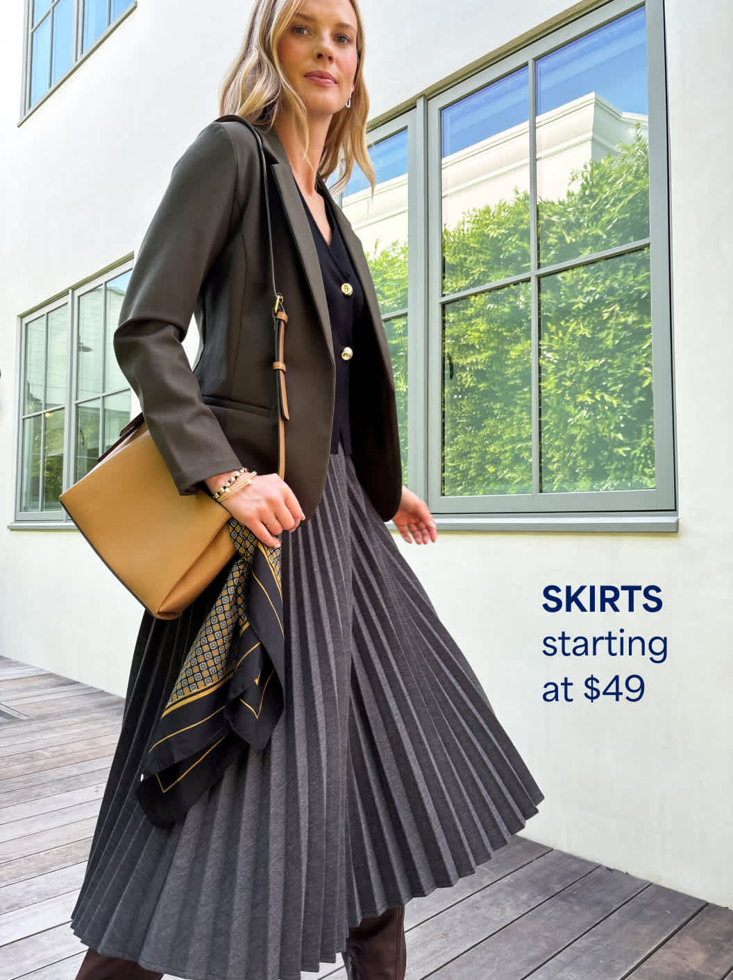 A Stitch Fix woman model posing and wearing a pleated skirt, along with a vest and blazer. Skirts starting at $49.