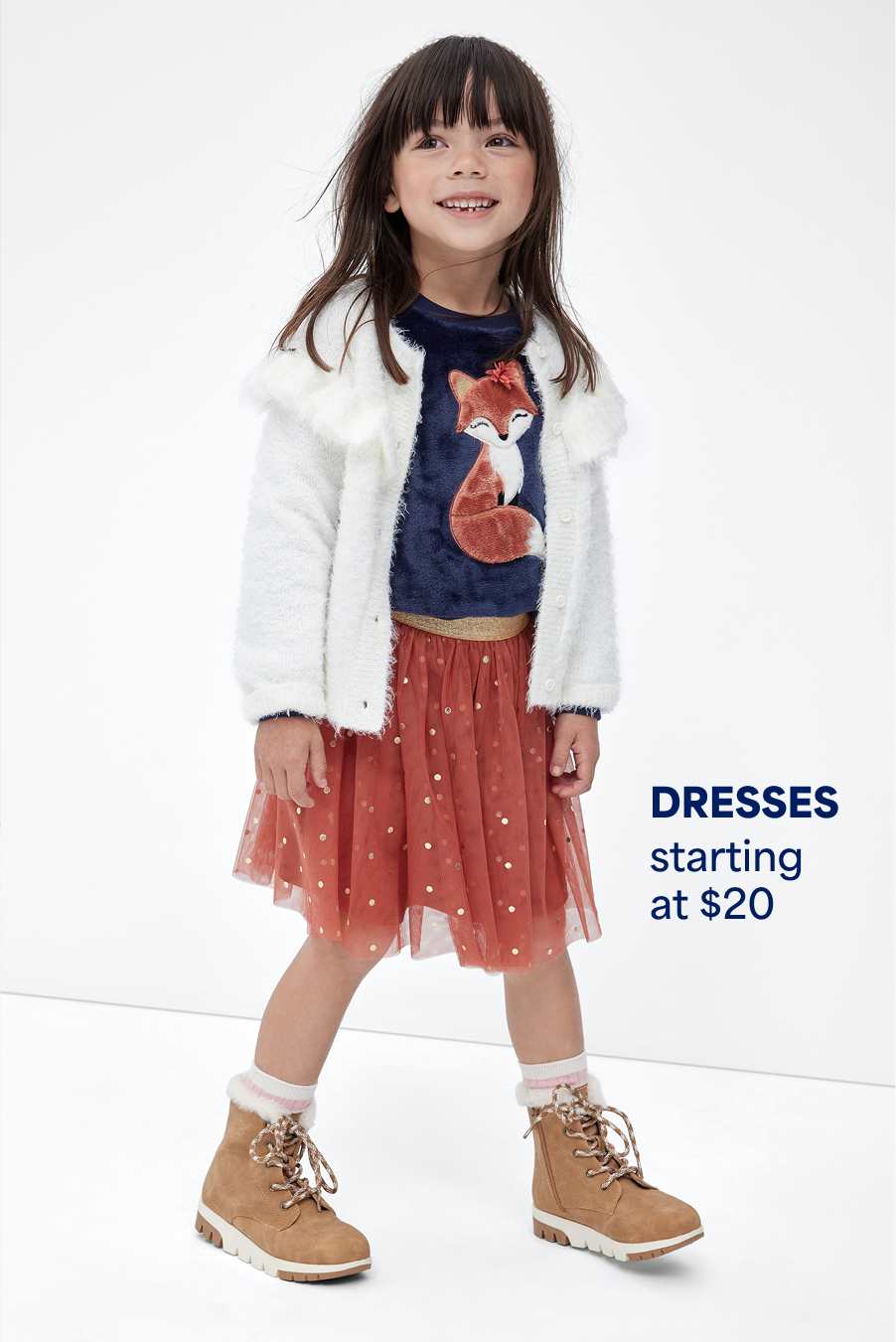 Stitch Fix young girl model smiling and wearing a multi-colored dress with a fox on it, fuzzy white sweater and tan boots. Text overlay on image reads “Dresses starting at $20”