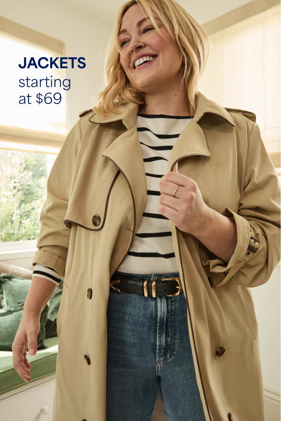 Stitch Fix woman model smiling and wearing a striped top, trench coat, jeans and black and gold belt. Text overlay on image reads “Jackets starting at $69”