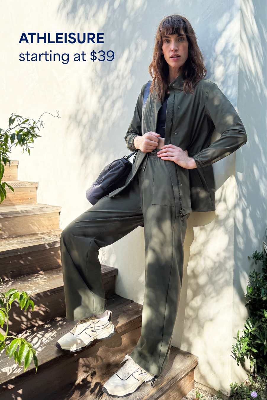 Stitch Fix woman model posing outside on steps wearing a green matching track set, black sports top, white active sneakers and black crossbody bag. Text overlay on image reads “Athleisure starting at $39”