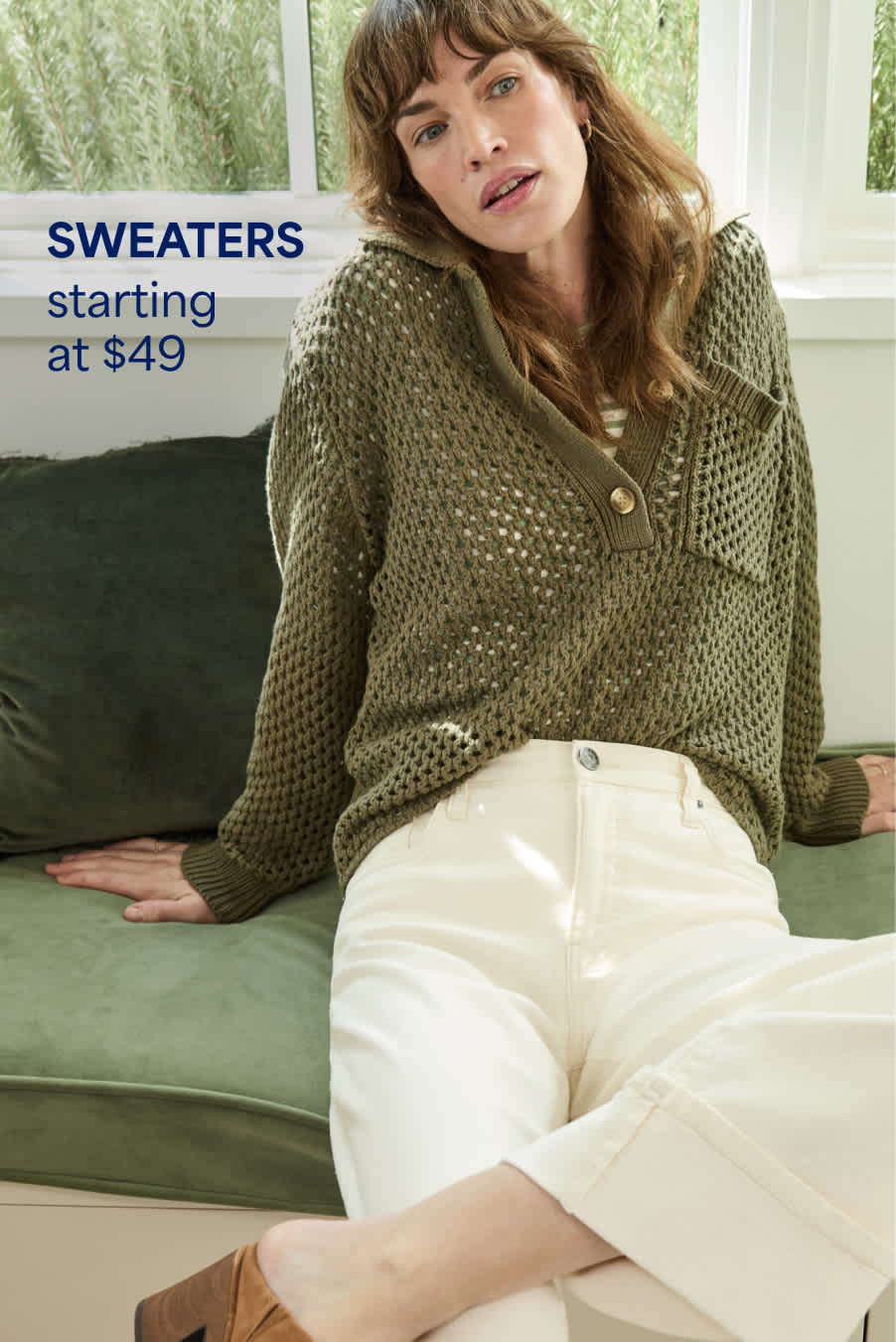 Stitch Fix woman model posing and sitting down on an indoor bench wearing a green crochet sweater, white jeans and sueded clogs. Text overlay on the image reads “Sweaters starting at $49”