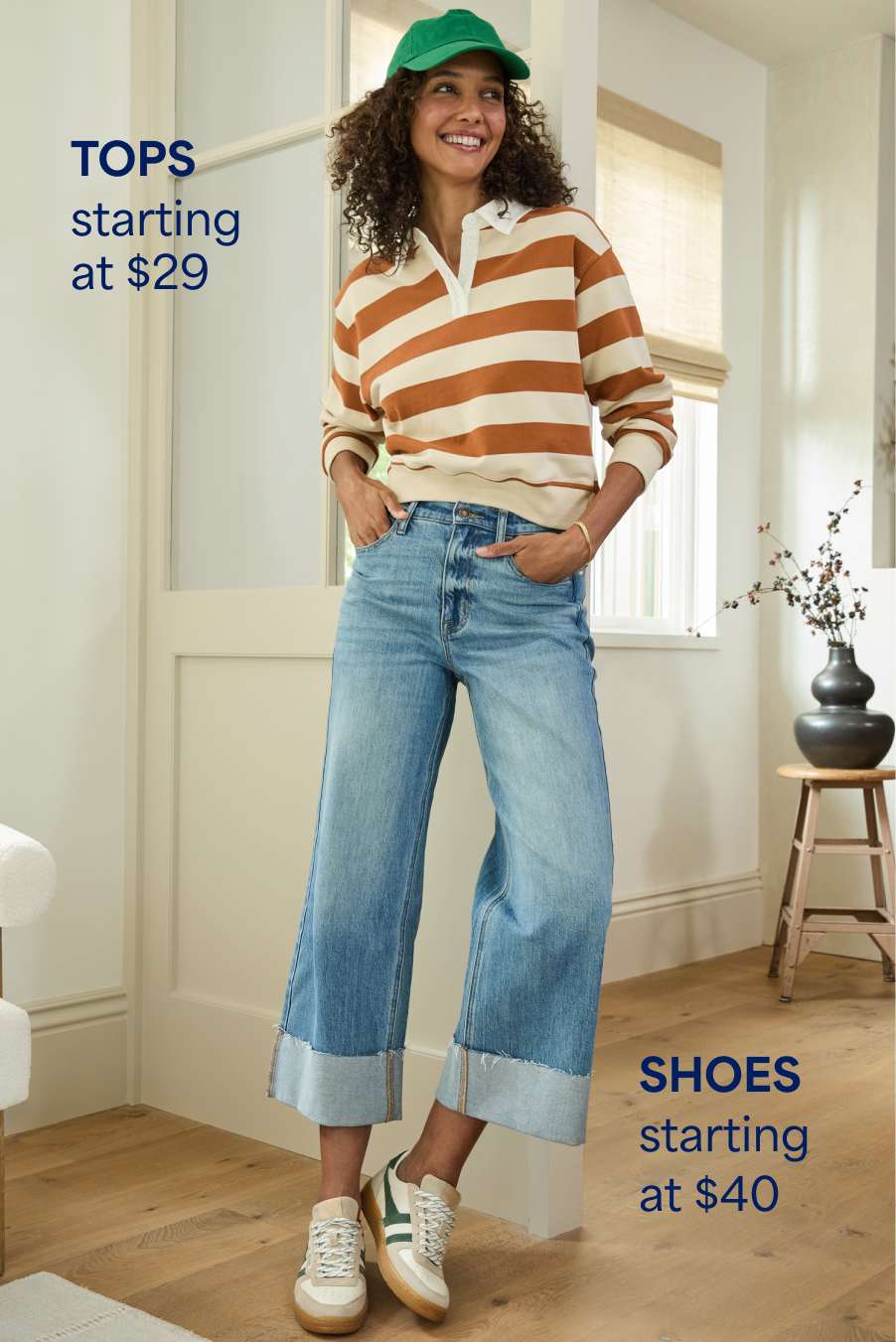 Stitch Fix woman model posing in a room in front of a window wearing a striped long-sleeve shirt and cuffed jeans. Text overlay on the image reads “Tops starting at $29” and “Jeans starting at $49”