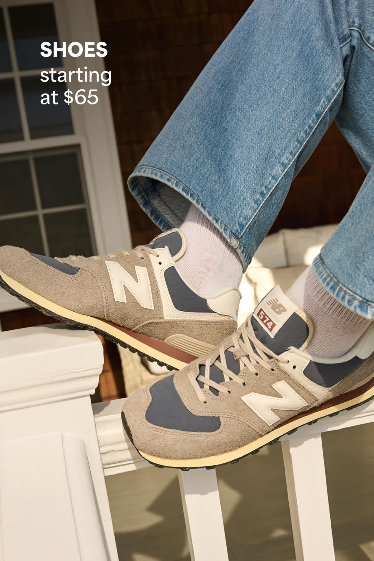 Close-up of a man’s feet resting on a porch railing, wearing suede sneakers with jeans and white socks. Text on the image reads “Shoes starting at $65,” highlighting the starting price for shoes.