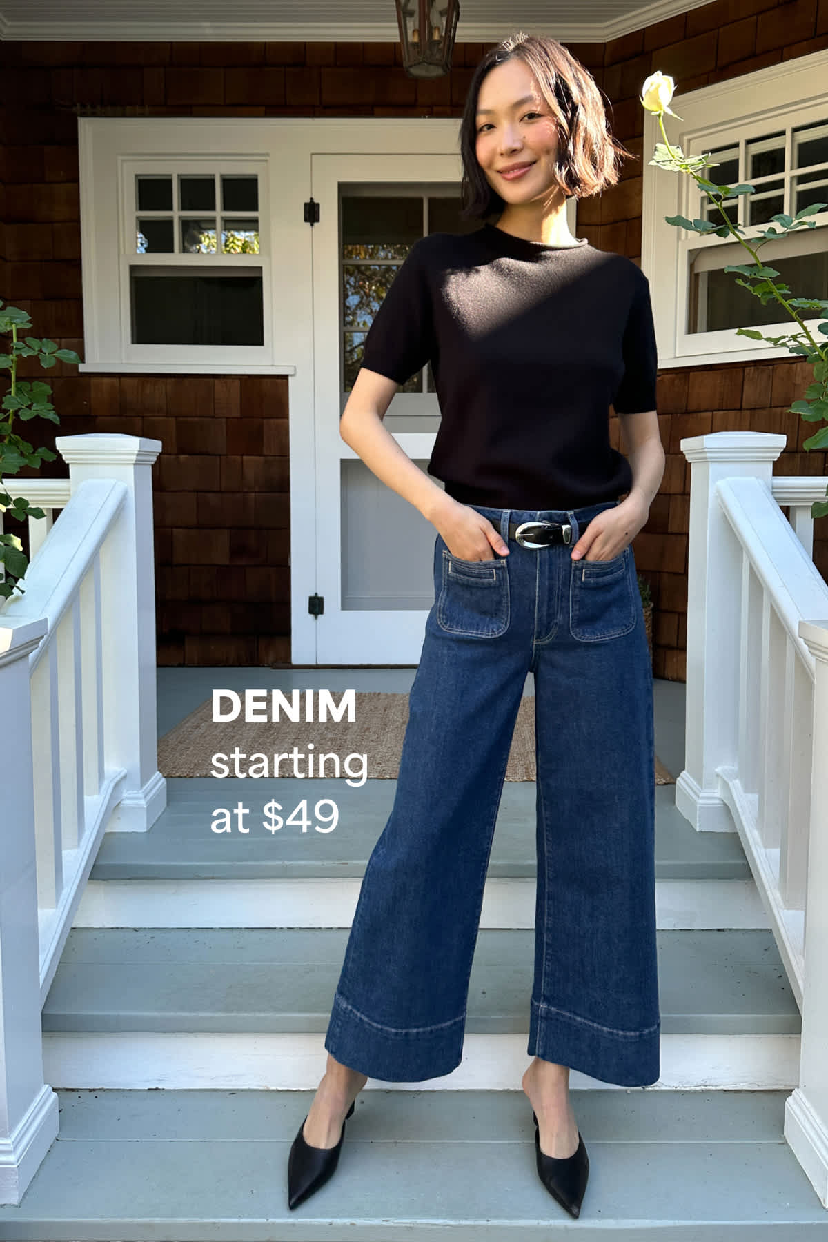 Woman standing on a porch wearing a black top and wide-leg jeans. Text reads “DENIM starting at $49.”