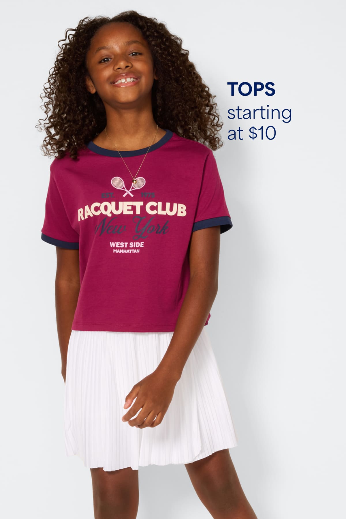 A smiling girl stands against a light background wearing a patterned blue dress layered with a cozy cardigan and brown sandals. Text on the image reads “Dresses starting at $20” and “Shoes starting at $10,” highlighting starting prices for kids’ dresses and shoes.