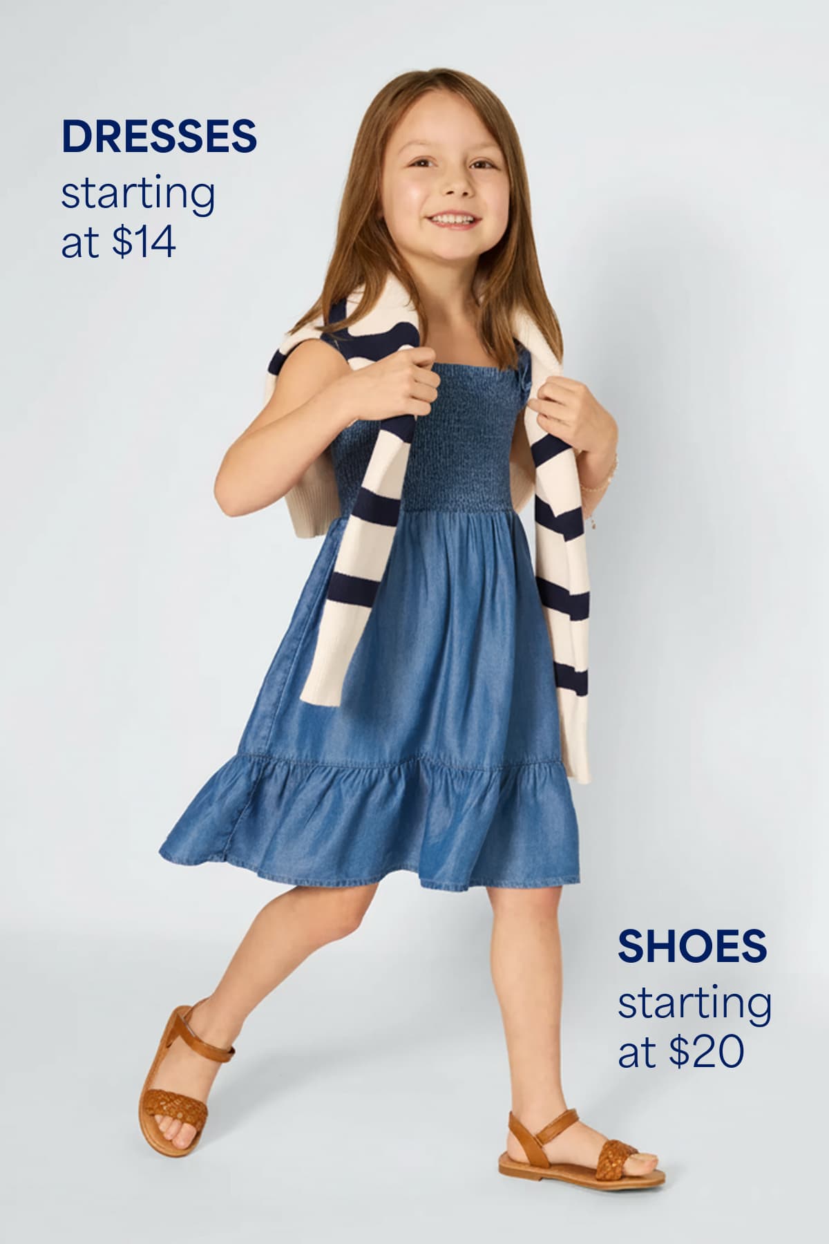 A smiling girl sits on a cushioned stool wearing a striped zip-up sweater layered over a top and a patterned skirt. Text on the image reads “Sweaters + Sweatshirts starting at $20,” highlighting the starting price for kids’ sweaters and sweatshirts.