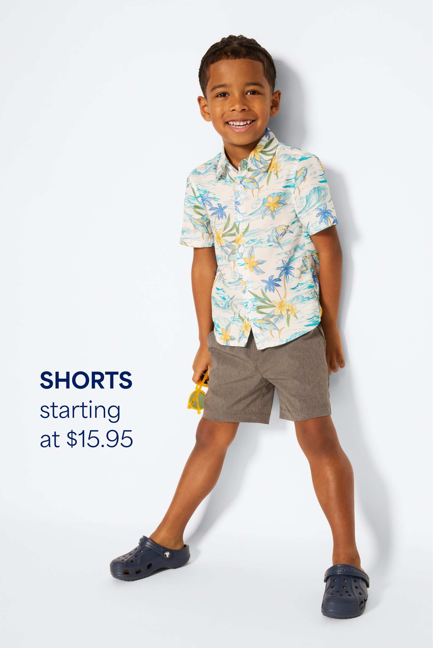 Stitch Fix young boy model sitting on a wooden block wearing a black, white and gray hoodie sweatshirt with joggers and checkered sneakers. Text overlay on image reads “Sweaters + sweatshirts starting at $20”