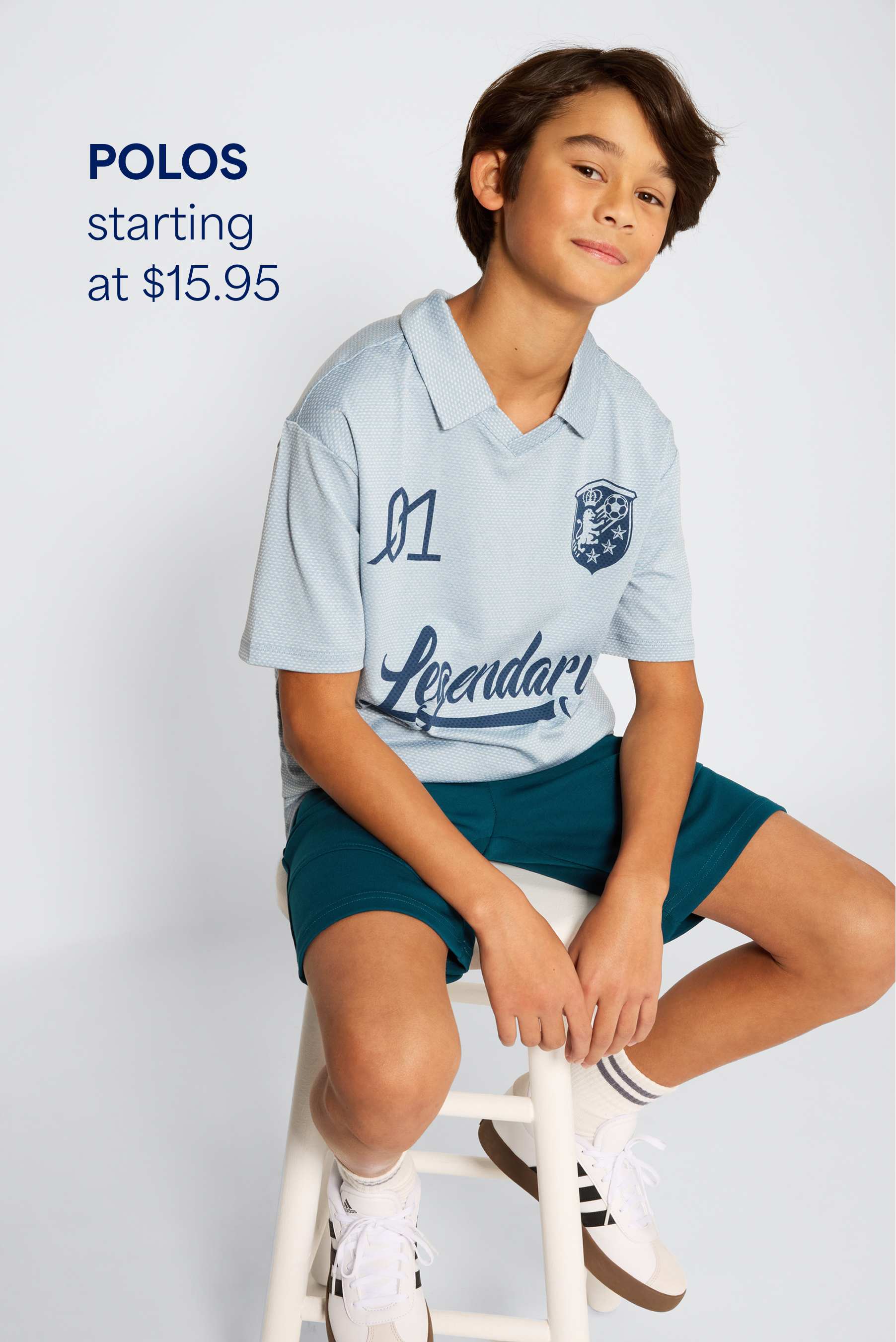 Stitch Fix young boy model smiling and wearing a blue beanie, green plaid flannel under a gray speckled hoodie and quilted green jacket, with dark-wash jeans and gray sneakers. Text overlay on image reads “Jeans + pants starting at $20”