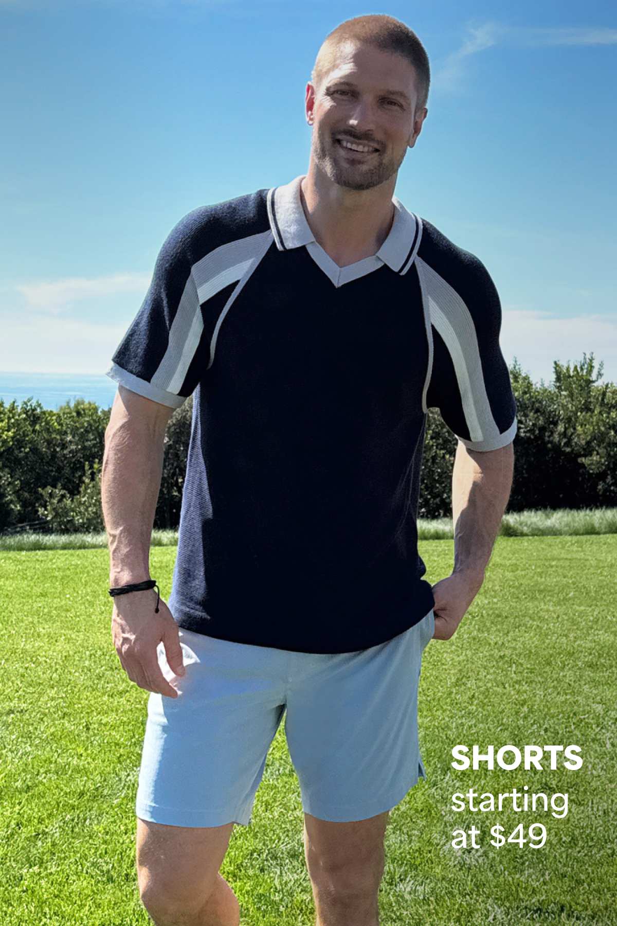 A man models a sporty navy polo and light blue shorts outdoors beside text that reads “SHORTS starting at $49.”