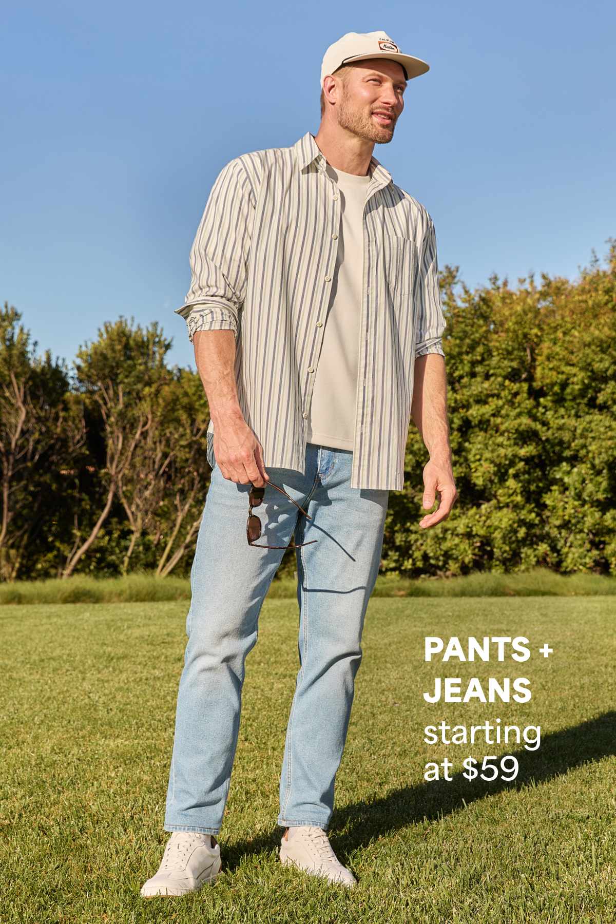 A man models a striped overshirt with a white tee and light denim jeans outdoors beside text that reads “PANTS JEANS starting at $59.”