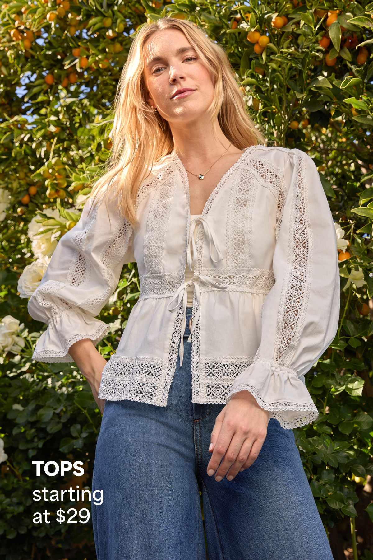 A woman models a white embroidered blouse with wide-leg denim outdoors beside text that reads “TOPS starting at $29.”