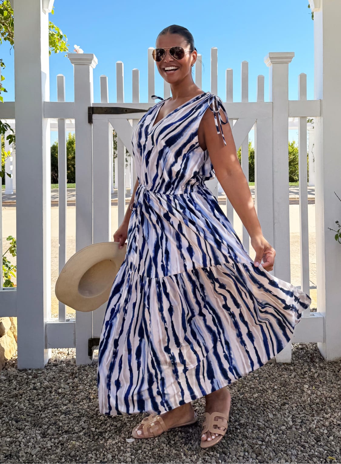 Woman in blue and white striped midi dress with tan sandals and straw hat