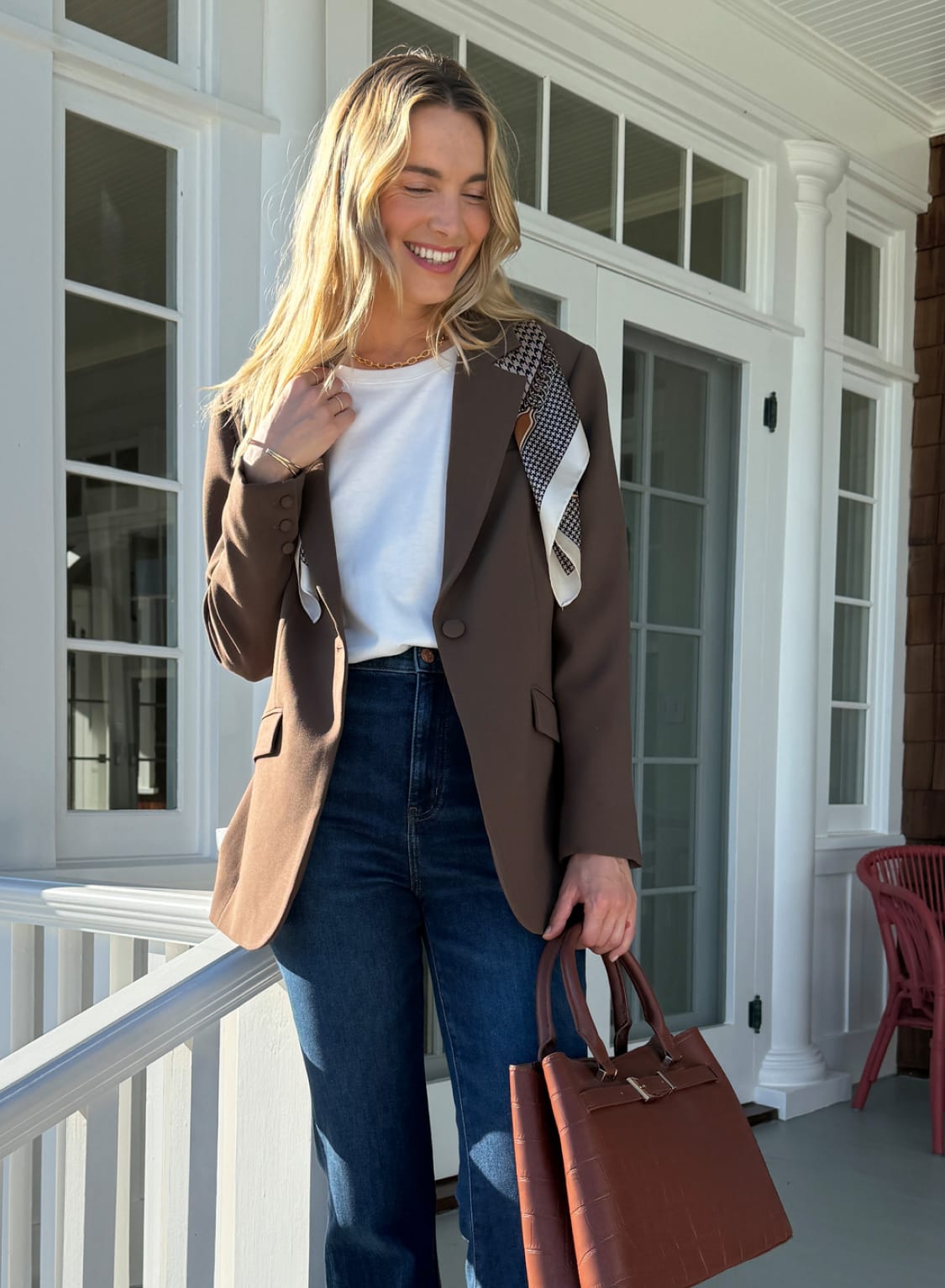Woman in brown blazer, white top and dark jeans holding brown tote bag