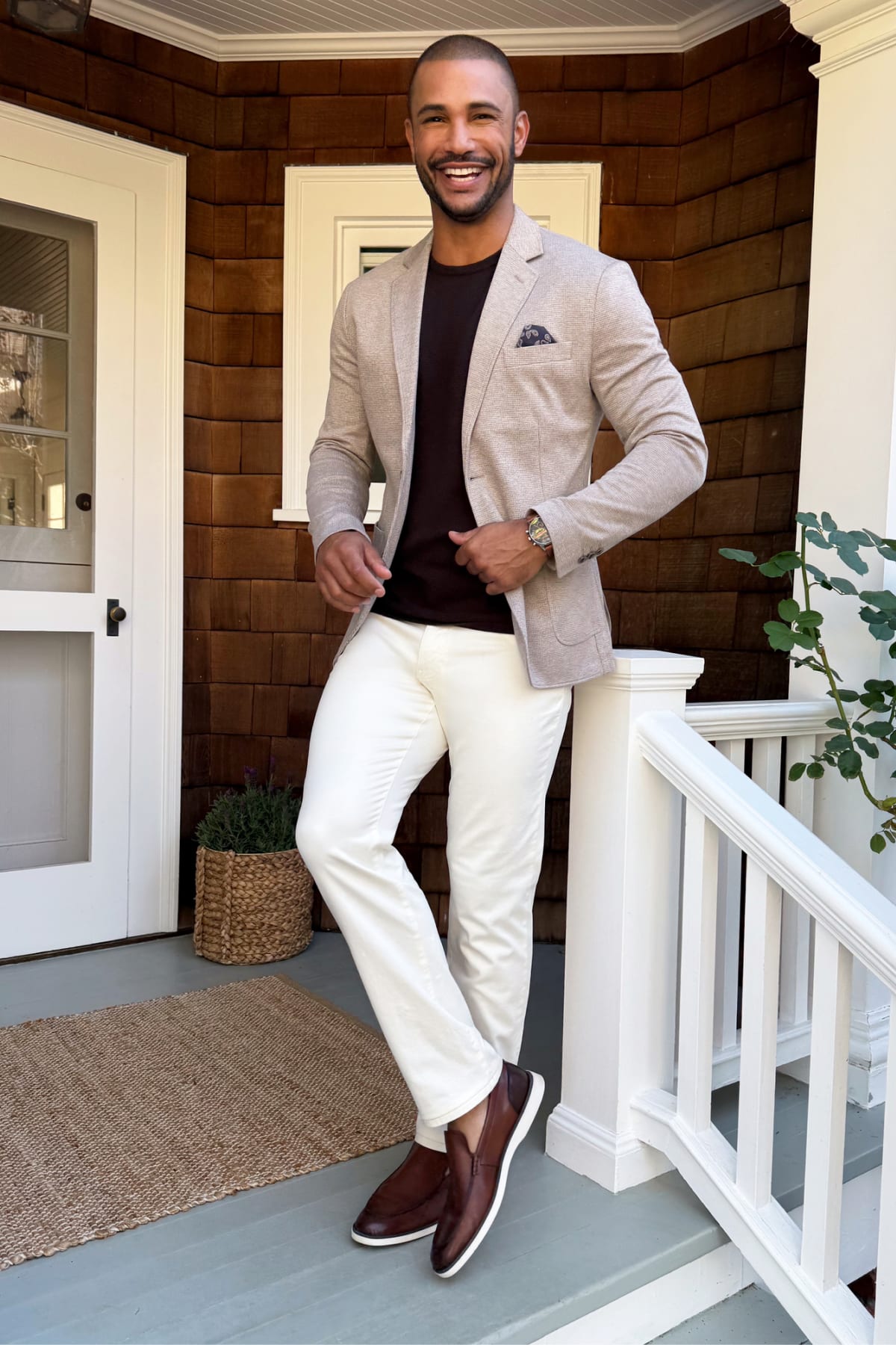 Model wearing Stitch Fix men’s clothes including a light gray blazer, dark T-shirt, white pants, and dark brown loafers.
