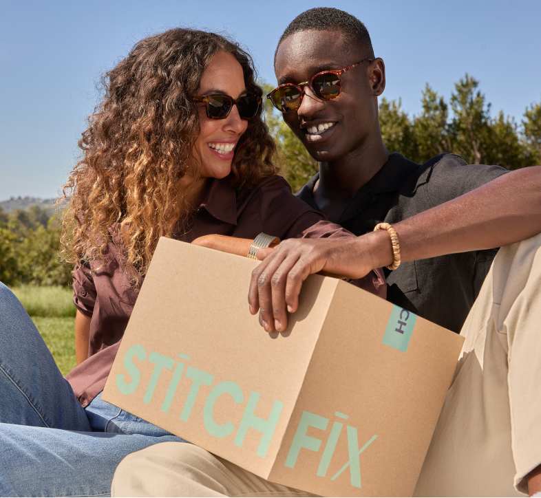 Woman in brown blouse, blue jeans, sunglasses; man in black shirt, beige pants, sunglasses, holding Stitch Fix box