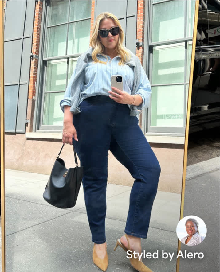 A Stitch Fix plus model taking a mirror selfie on the street. She’s wearing a blue button-down, dark straight-leg jeans, tan heels and a black bucket bag. There’s a small image overlay in the bottom right hand corner of a woman Stylist with the text “Styled by Alero”