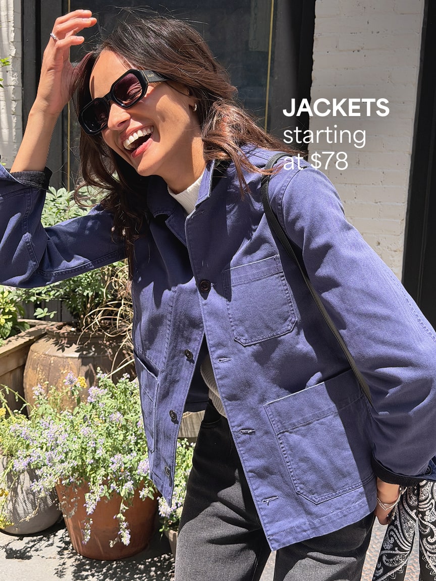 Woman wearing a blue jacket over a white top, dark pants, sunglasses, carrying a black shoulder bag. Jackets starting at $78
