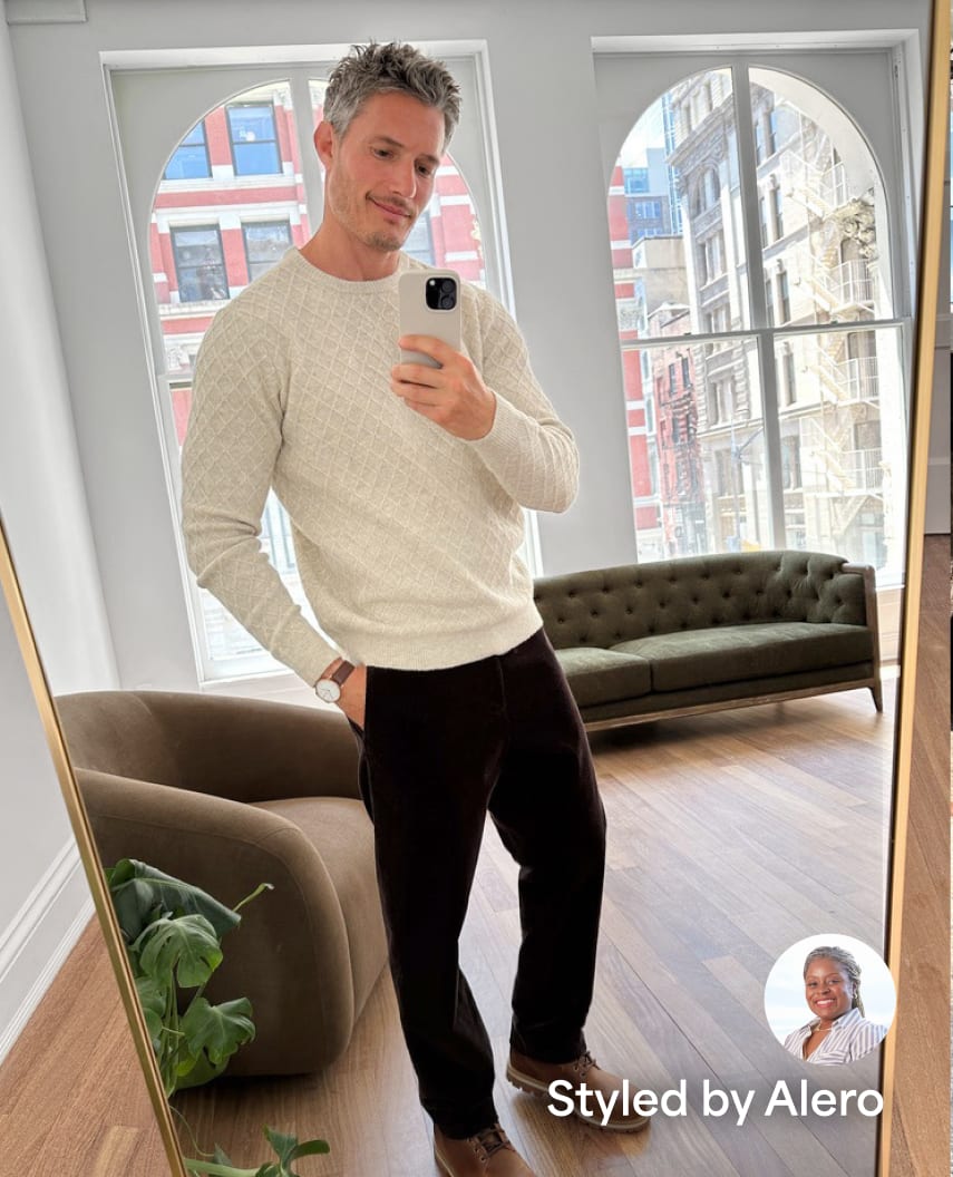 Man taking a mirror selfie wearing an off-white textured long-sleeve sweater, dark brown trousers, and brown shoes