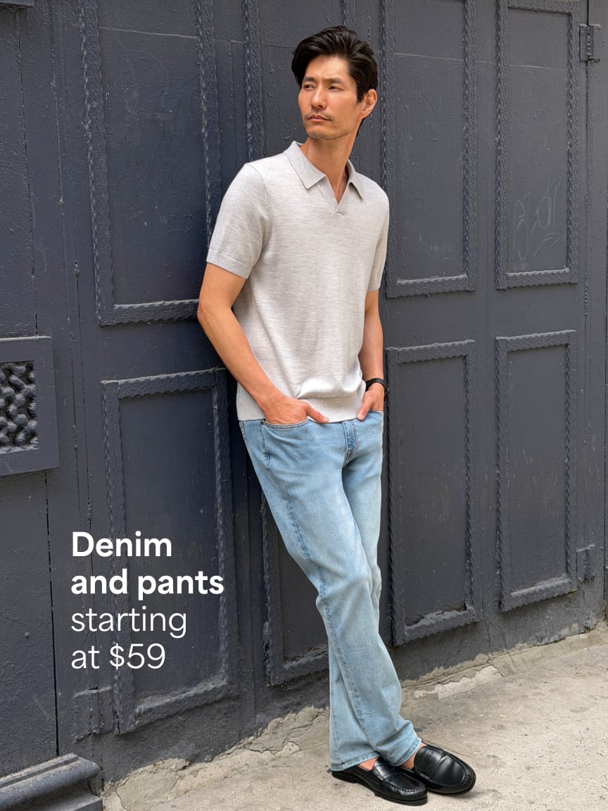 Man leaning against wall wearing light grey short-sleeve polo shirt, light blue jeans, black loafers. Text: Denim and pants starting at $59