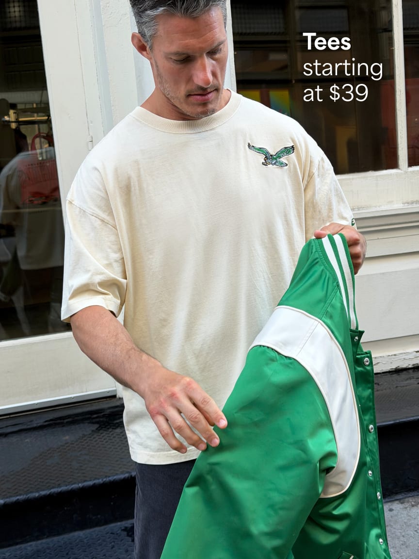 Man holding a green jacket over a white t-shirt with dark grey pants. Text: Tees starting at $39