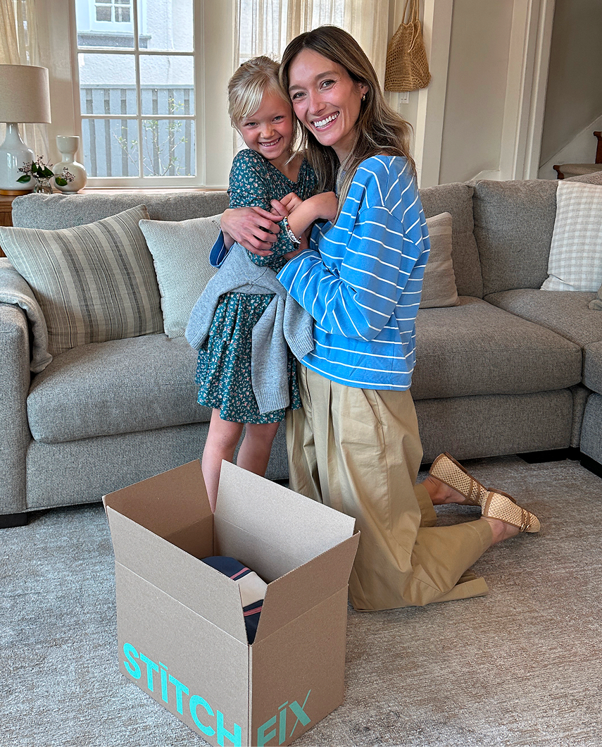 Woman in blue striped top and tan pants with a child in green floral dress, kneeling beside an open Stitch Fix box
