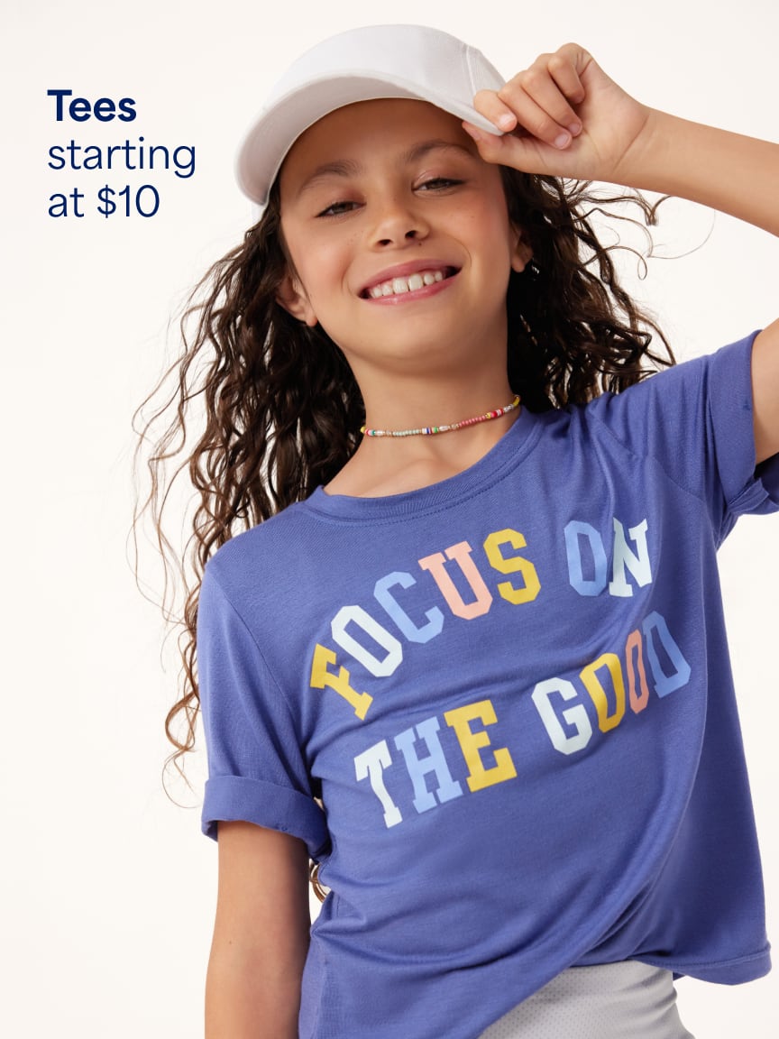 Child wearing a purple graphic t-shirt reading Focus On The Good and a white baseball cap. Text: Tees starting at $10