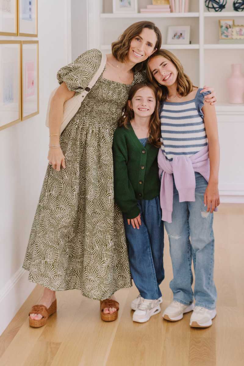 Model wearing Stitch Fix women's clothes including a green printed maxi dress and tan platform sandals, with kids wearing Stitch Fix kids' clothes including a green cardigan, a blue striped top, and light wash jeans.