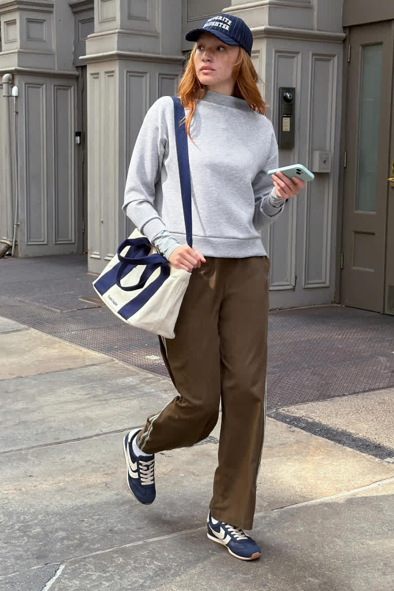 Model wearing Stitch Fix women's clothes including a gray sweatshirt, brown pants, a navy baseball cap, and navy sneakers.