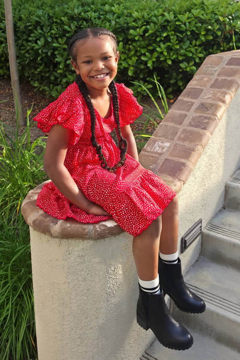 Model wearing Stitch Fix kids' clothes including a red polka-dot dress and black ankle boots.