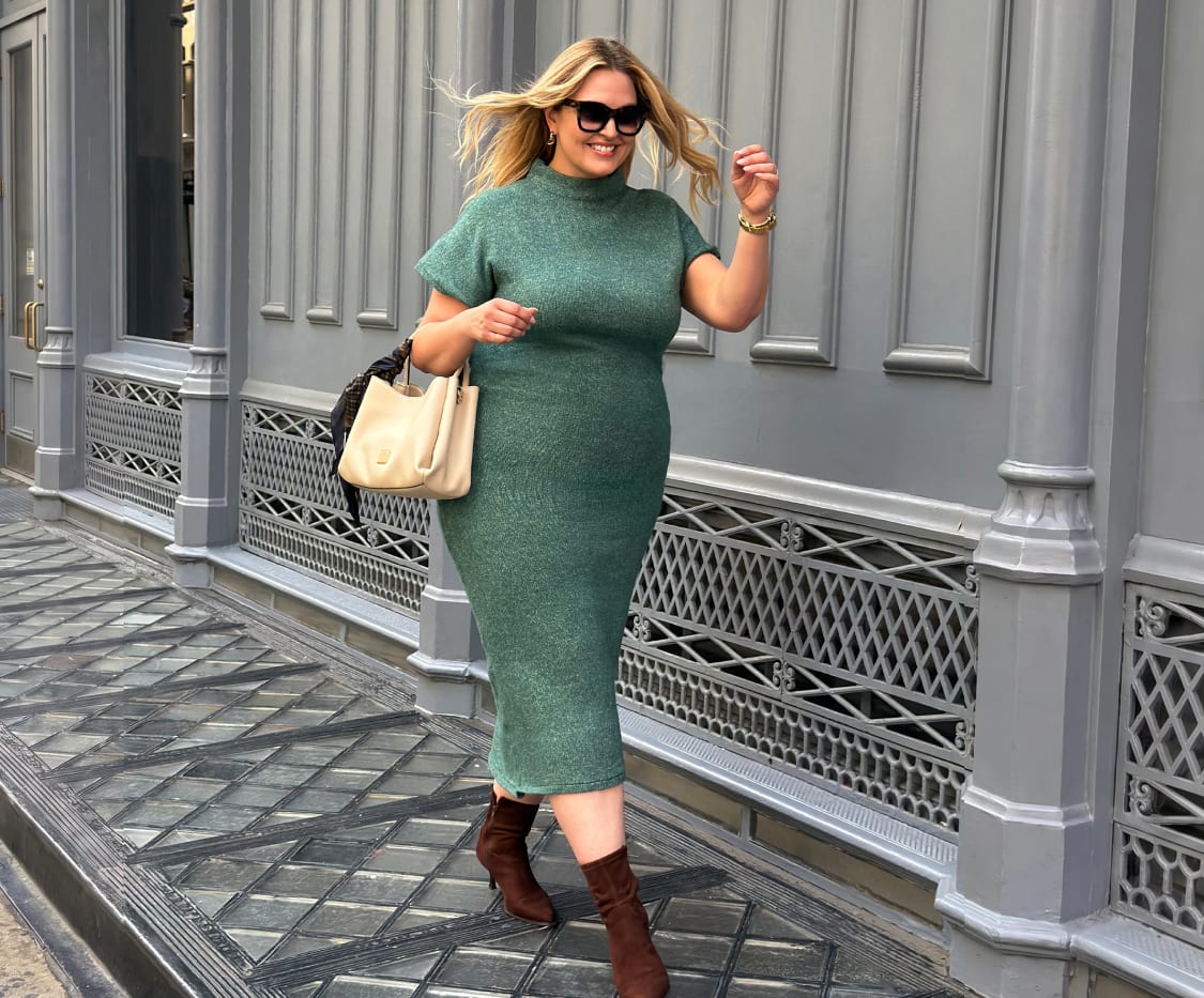 Woman wearing a green short-sleeve turtleneck midi dress, brown ankle boots, sunglasses, carrying a cream tote bag