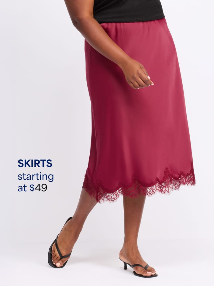 Woman wearing red satin midi skirt with lace hem trim, black top, and black thong sandal heels. Skirts starting at $49