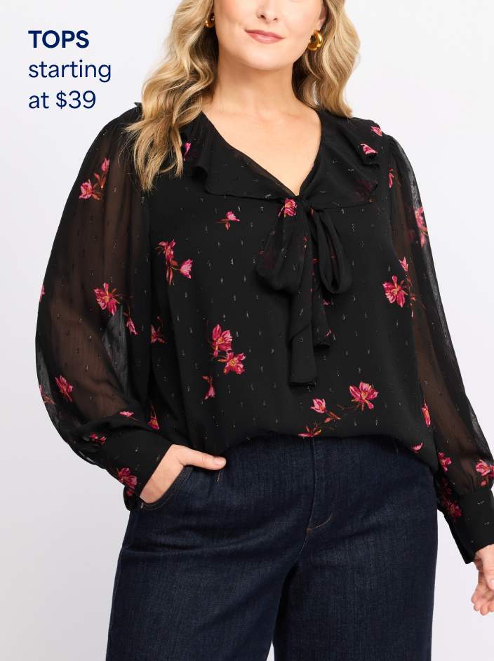Woman wearing black long-sleeve blouse with pink floral print and dark denim jeans. Tops starting at $39