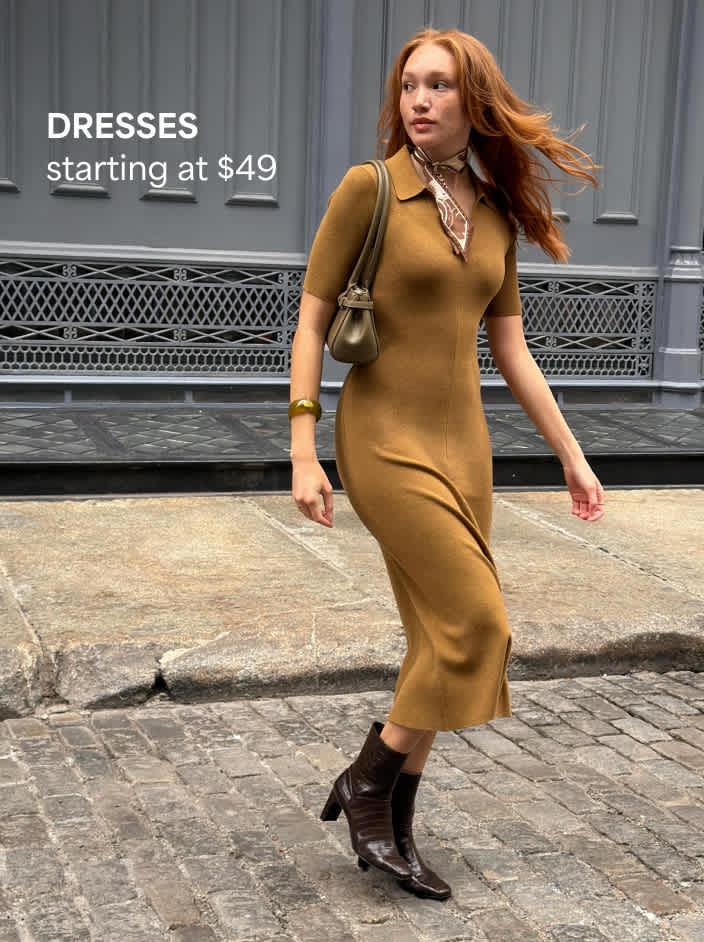 Woman walking wearing a mustard yellow polo midi dress, patterned neck scarf, brown boots, and a brown shoulder bag