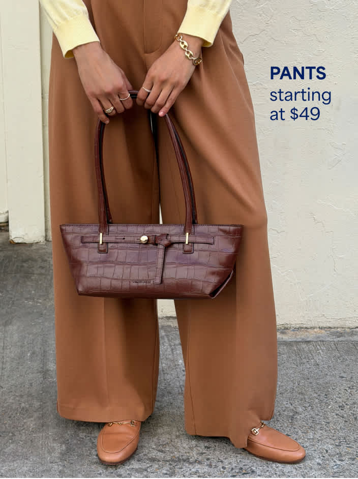 Woman wearing wide-leg tan trousers, tan loafers, yellow top, holding dark brown leather shoulder bag
